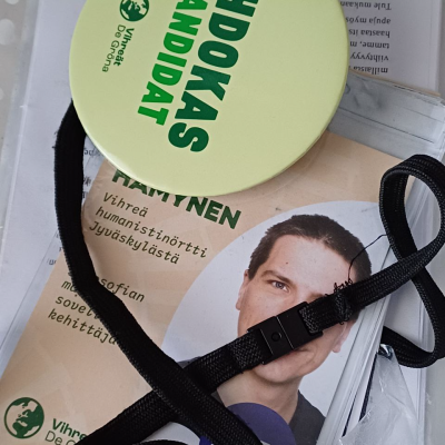 Ehdokaspinssi ja vaaliflyeri kaulanauhassa.
